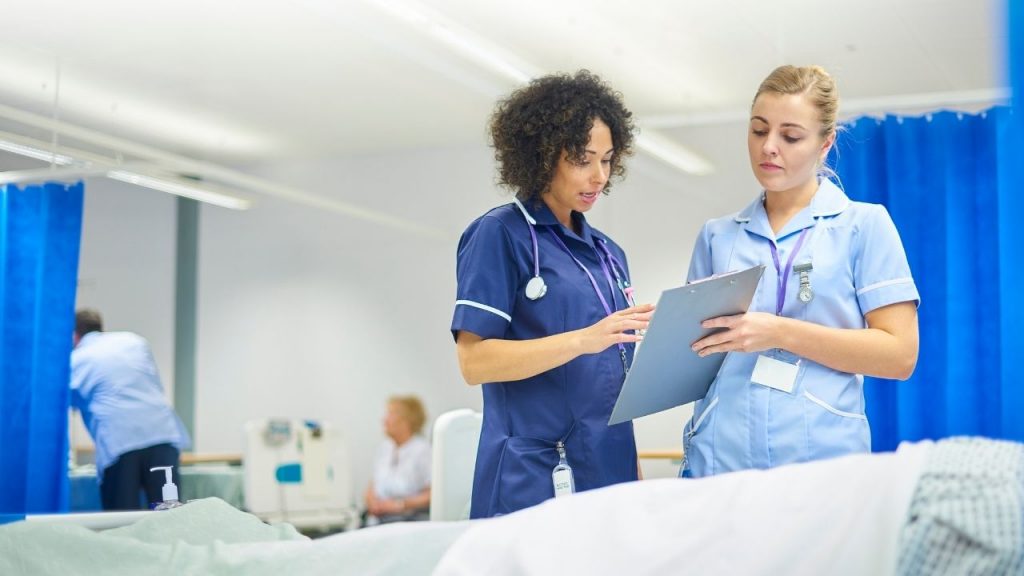 kaksi sairaanhoitajaa keskustelemassa ja tekemässä muistiinpanoja
